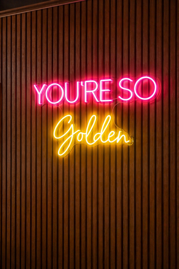 Neon “You’re So Golden” sign on timber wall near spray tanning booth